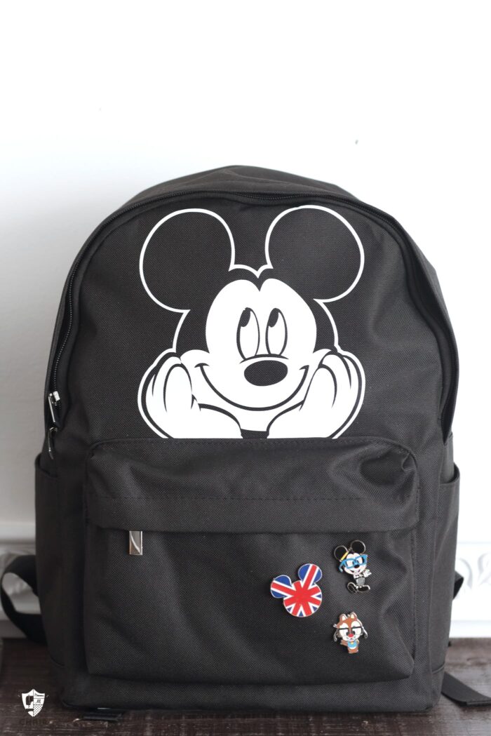 black backpack with mickey mouse iron on sitting on table in front of white wall