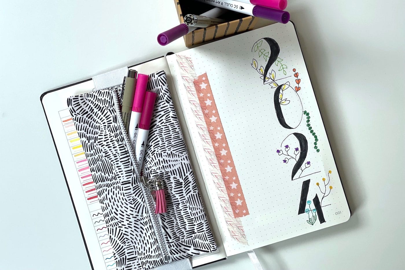 black and white pencil pouch on black notebook on table with colorful pens and pencils