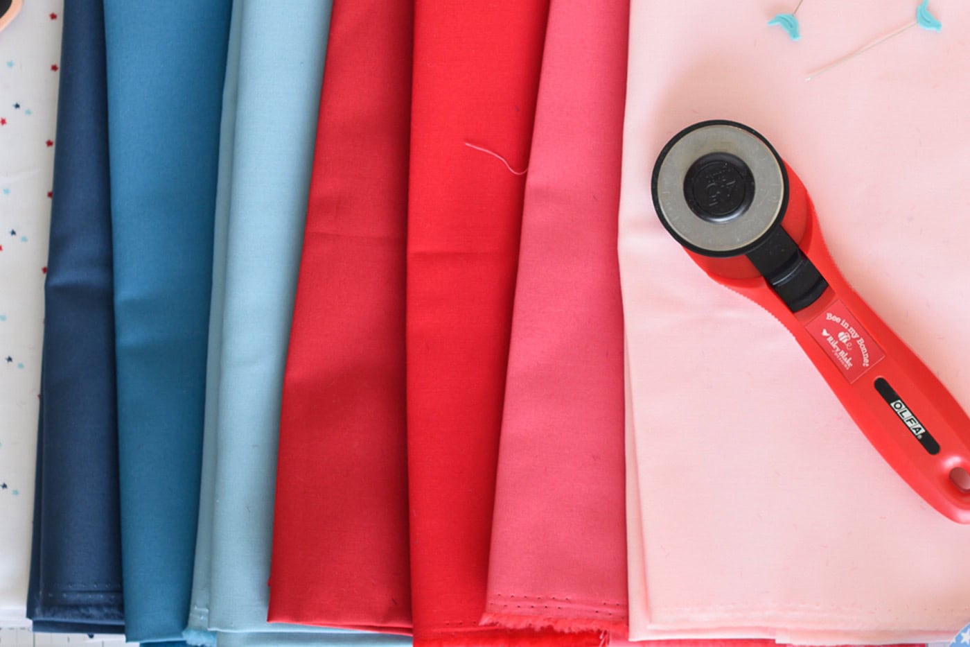 red, blue and pink fabric with red rotary cutter