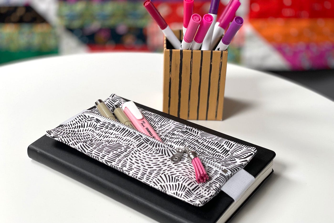 black and white pencil pouch on black notebook on table with colorful pens and pencils