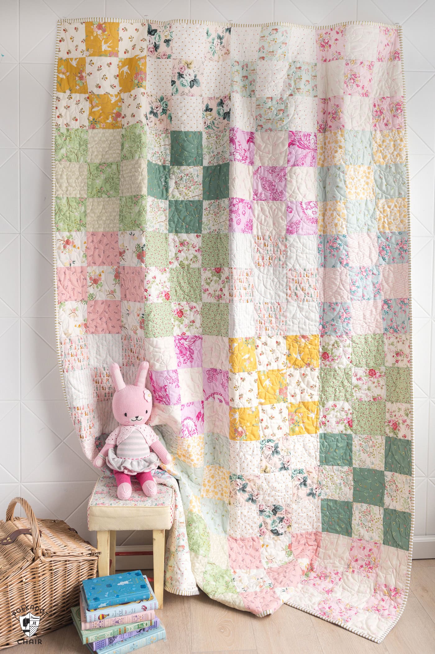 pink, green, yellow and ivory patchwork quilt on wall with toys in the foreground