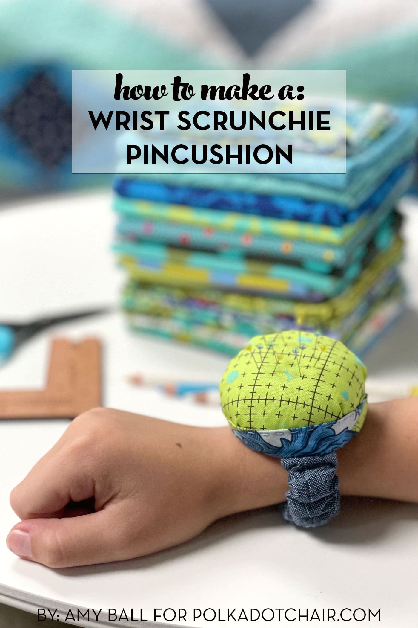 image of pincushion on wrist in front of stack of colorful fabrics