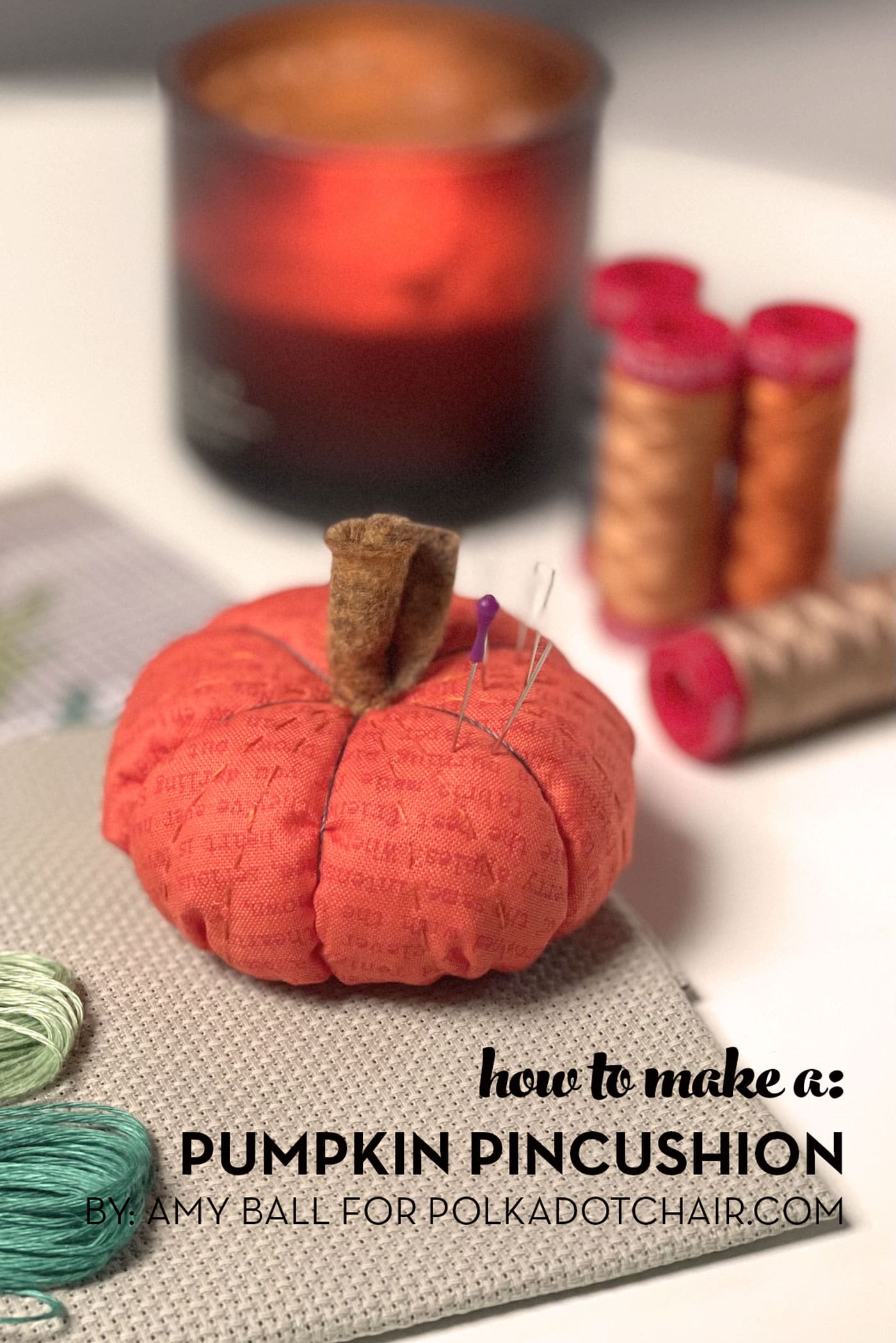 pumpkin pinucushion on table with sewing notions and candle